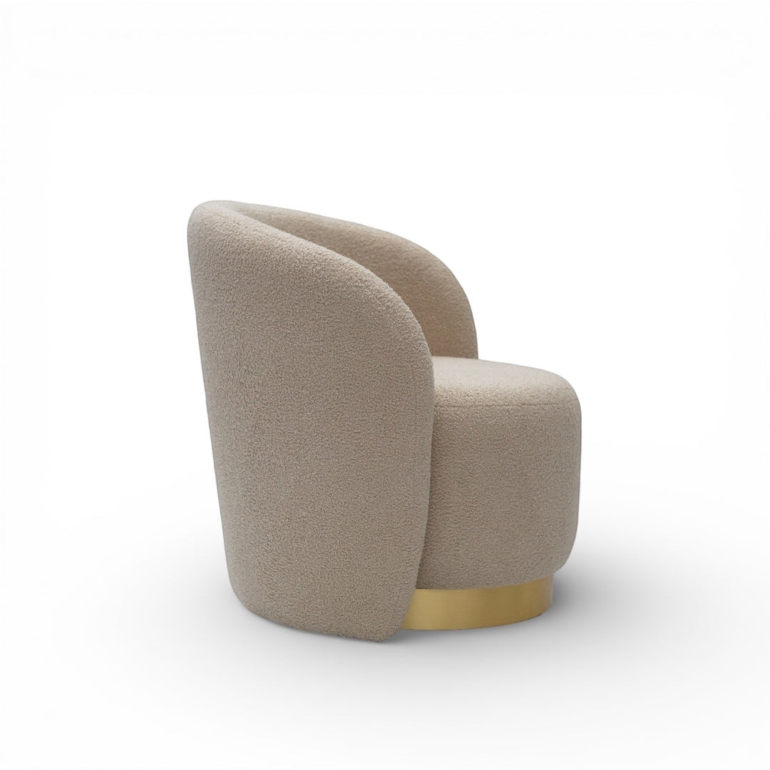 Side angled view of the Vaya Home Cocoon accent chair featuring beige boucle upholstery, a rounded sculptural back, and gold base trim.
