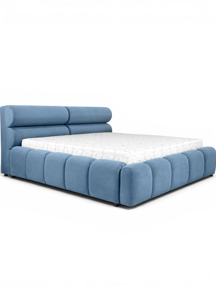 Front angled view of the Vaya Home Como bed with blue upholstery, a padded headboard, and a low platform frame with channel detailing.