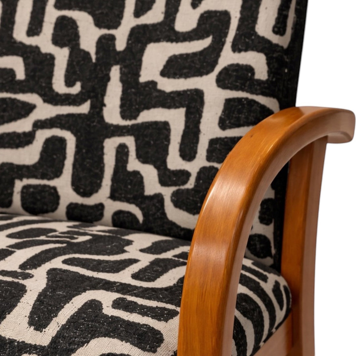 Close-up of the Vaya Home Contour accent chair showing the curved wood armrest and black-and-cream abstract patterned upholstery.