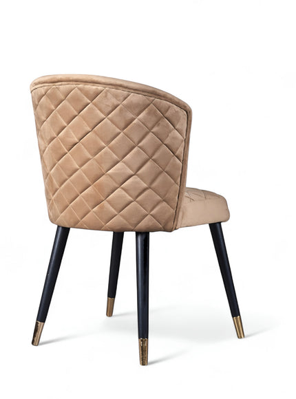 Rear angled view of the Vaya Home Diamante dining chair featuring beige upholstery, diamond-quilted back detail, and black tapered legs with gold caps.