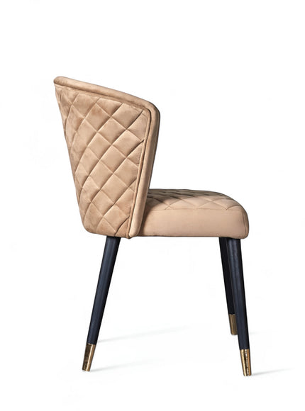 Side view of the Vaya Home Diamante dining chair with beige upholstery, diamond-quilted backrest, and black tapered legs with gold caps.