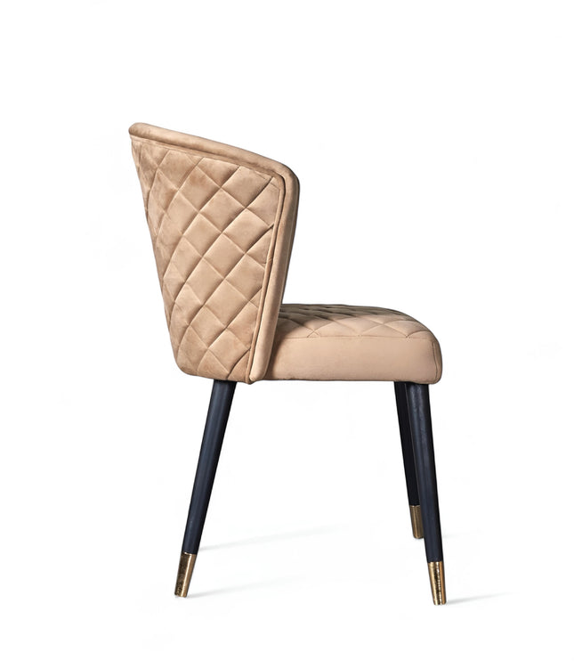 Side view of the Vaya Home Diamante dining chair with beige upholstery, diamond-quilted backrest, and black tapered legs with gold caps.