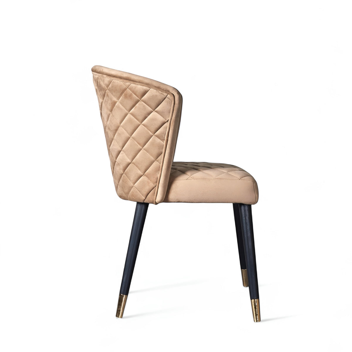 Side view of the Vaya Home Diamante dining chair with beige upholstery, diamond-quilted backrest, and black tapered legs with gold caps.