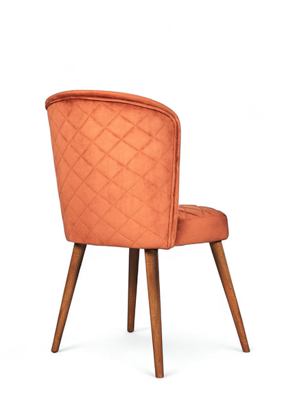 Rear angled view of the Vaya Home Inverto dining chair showing orange upholstery, quilted backrest detail, and wood legs with gold caps.