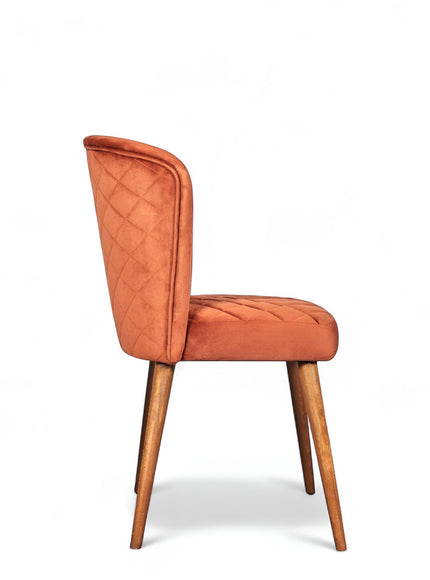Side view of the Vaya Home Inverto dining chair with orange upholstery, quilted back detail, and tapered wood legs with gold caps.