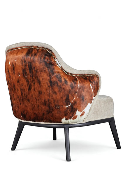 Rear angled view of the Vaya Home Kalv accent chair with a brown cowhide outer back, beige upholstered seat, and black legs.