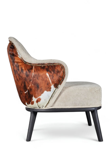 Side view of the Vaya Home Kalv accent chair featuring beige upholstery, brown cowhide outer back, curved arms, and black legs.