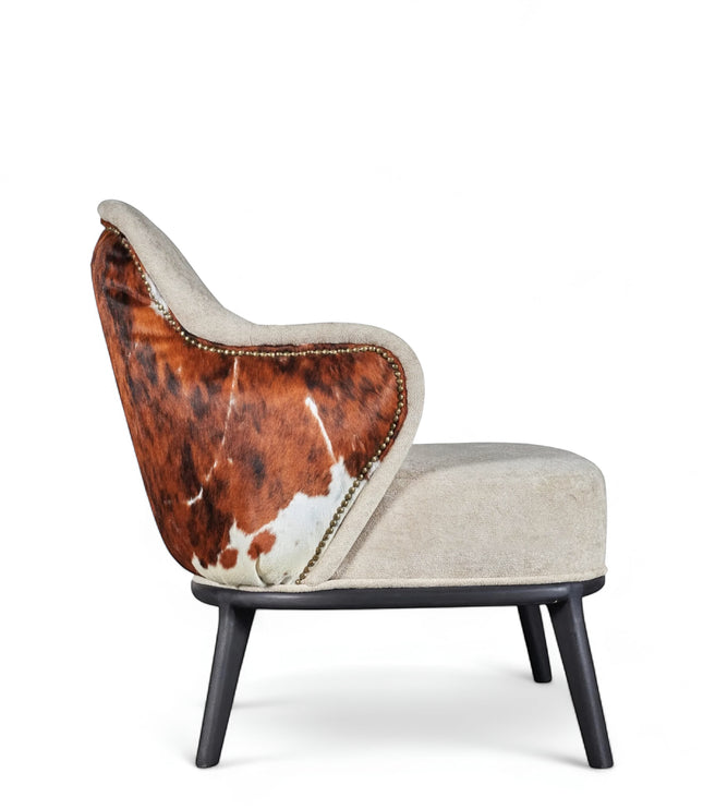Side view of the Vaya Home Kalv accent chair featuring beige upholstery, brown cowhide outer back, curved arms, and black legs.