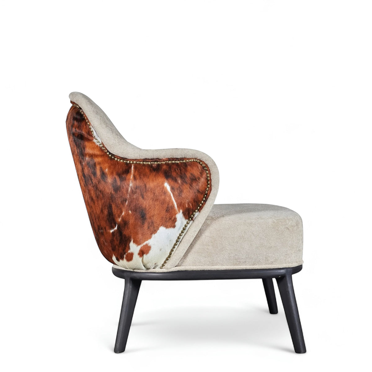 Side view of the Vaya Home Kalv accent chair featuring beige upholstery, brown cowhide outer back, curved arms, and black legs.