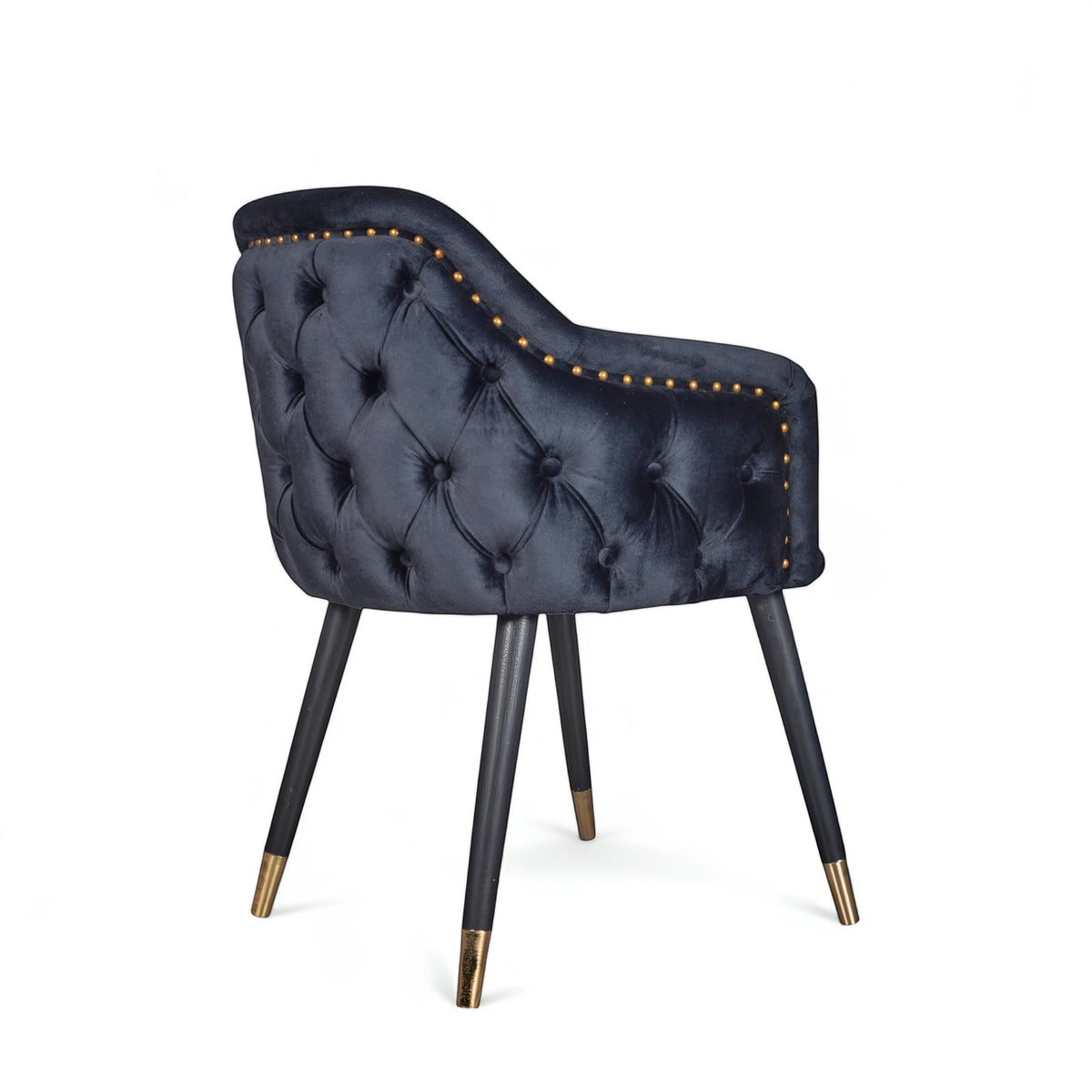 Rear angled view of the Vaya Home Lila accent chair featuring dark blue velvet upholstery, nailhead trim, tufted back detail, and black legs with gold caps.