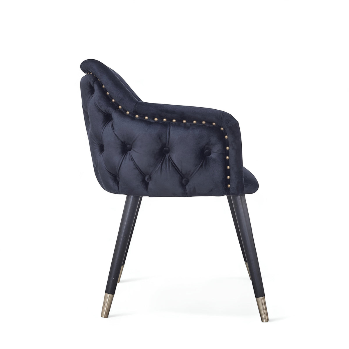 Side view of the Vaya Home Lila accent chair with dark blue velvet upholstery, button-tufted back, nailhead trim, and black legs with gold caps.