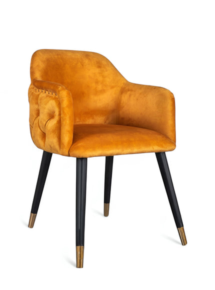 Product view of the Vaya Home Lila accent chair in orange velvet upholstery with nailhead trim and black legs with gold caps.