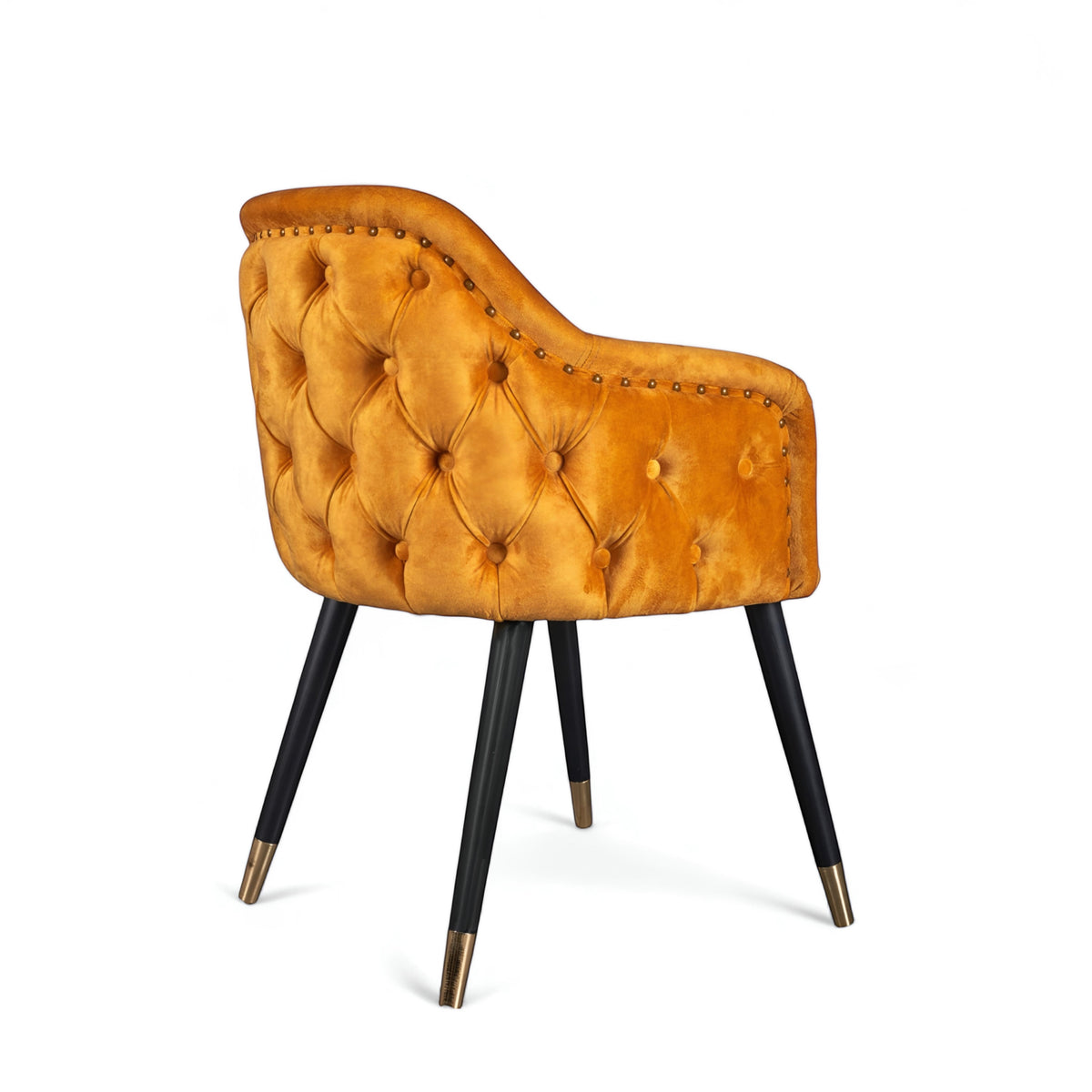 Side view of the Vaya Home Lila accent chair with orange velvet upholstery, button-tufted back, nailhead trim, and black legs with gold caps.