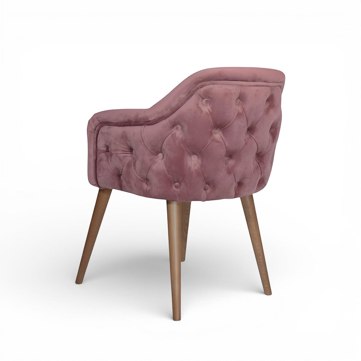 Rear angled view of the Vaya Home Lila accent chair featuring pink velvet upholstery, button-tufted back detail, and tapered wood legs.
