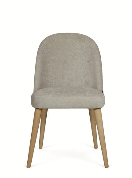 Rear angled view of the Vaya Home Limett dining chair featuring beige upholstery, a softly curved back, and tapered wood legs.
