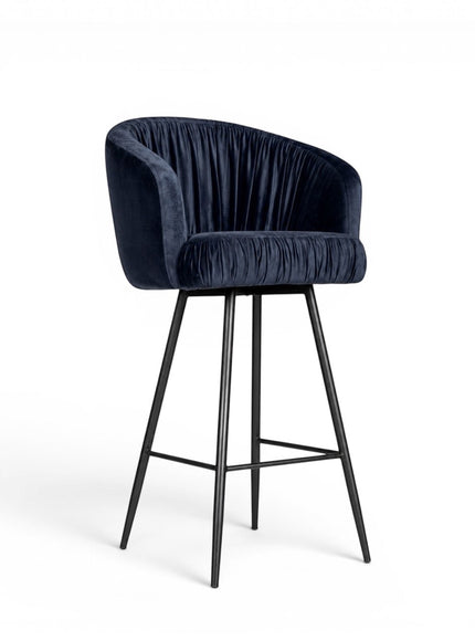 Front angled view of the Vaya Home Midnight bar stool with dark blue velvet upholstery, a channel-tufted curved back, and a black metal base.
