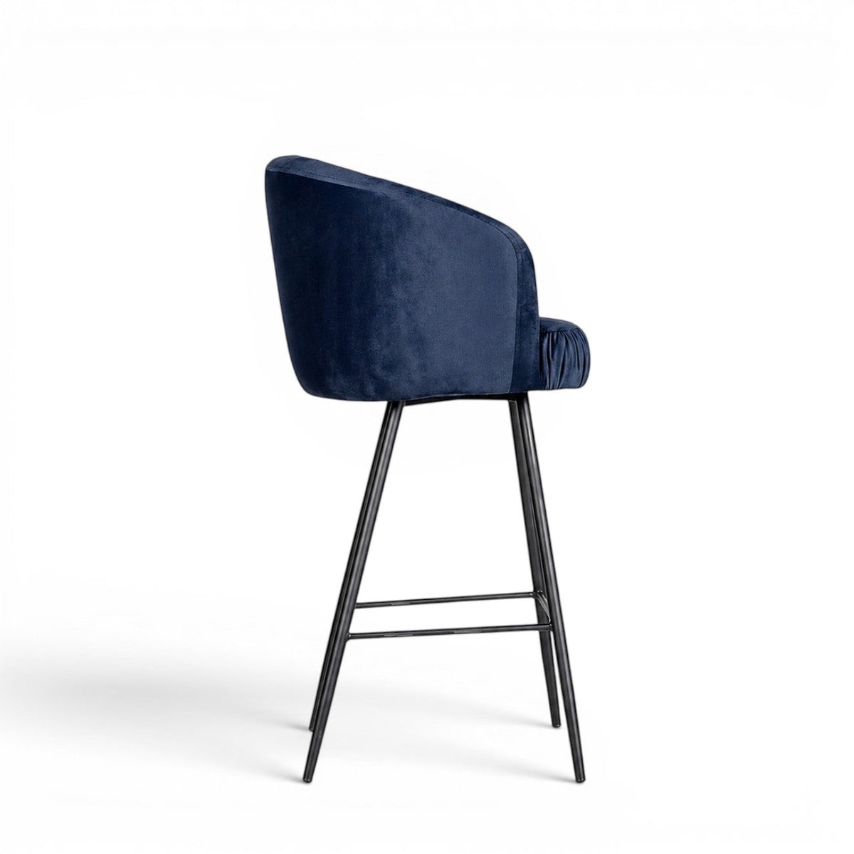 Side view of the Vaya Home Midnight bar stool featuring dark blue velvet upholstery, a curved backrest, and a black metal base.