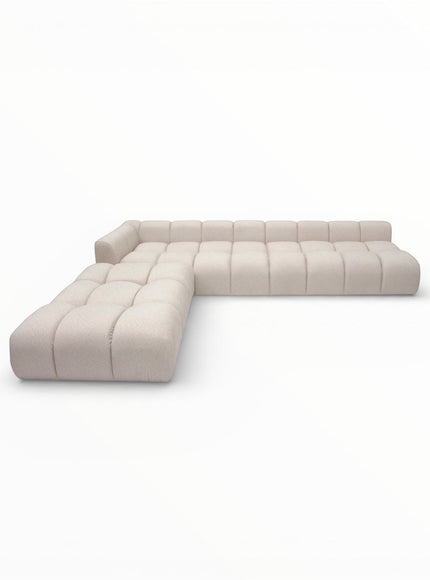 Angled view of the Vaya Home Monolith L-shaped modular sectional sofa with cream upholstery and channel-tufted cushioning.