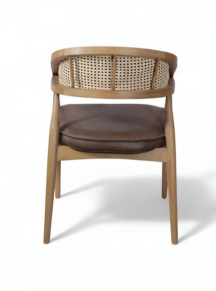 Rear angled view of the Vaya Home Morbido dining chair with a woven cane back, dark brown seat cushion, and curved wood frame.