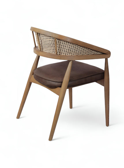 Rear angled view of the Vaya Home Morbido dining chair with a woven cane back, dark brown seat cushion, and curved wood frame.