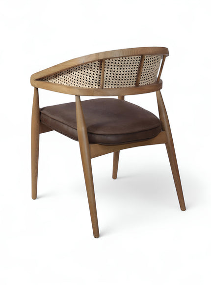 Rear angled view of the Vaya Home Morbido dining chair with a woven cane back, dark brown seat cushion, and curved wood frame.