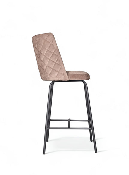 Side view of the Vaya Home Morkrod bar stool featuring beige quilted upholstery and black metal legs.