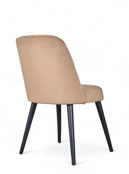 Rear angled view of the Vaya Home Netto dining chair featuring beige upholstery, a softly curved backrest, and black tapered legs.