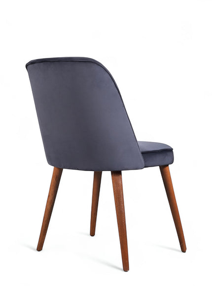 Rear angled view of the Vaya Home Netto dining chair featuring dark blue upholstery, a softly curved backrest, and tapered wood legs.