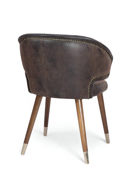 Opposite rear angled view of the Vaya Home Pelle accent chair with dark brown upholstery, nailhead trim, and tapered wood legs with metal caps.