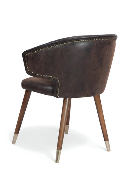 Rear angled view of the Vaya Home Pelle accent chair with dark brown leather-look upholstery, curved back, and tapered wood legs with metal caps.