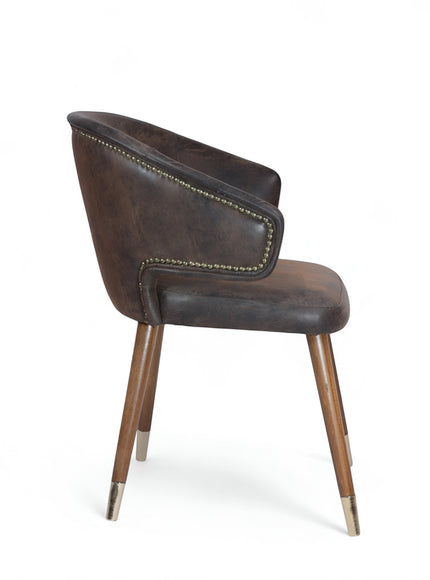 Side view of the Vaya Home Pelle accent chair with dark brown leather-look upholstery, curved back, nailhead trim, and tapered wood legs with metal caps.