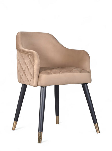 Front angled view of the Vaya Home Pino dining chair with beige upholstery, curved arms, and black tapered legs with gold caps.