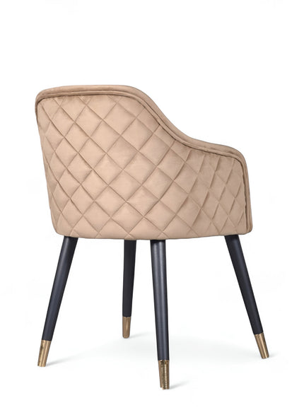 Rear angled view of the Vaya Home Pino dining chair featuring beige upholstery, diamond-quilted back detail, and black tapered legs with gold caps.