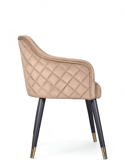 Side view of the Vaya Home Pino dining chair with beige upholstery, curved arm detail, and black tapered legs with gold caps.