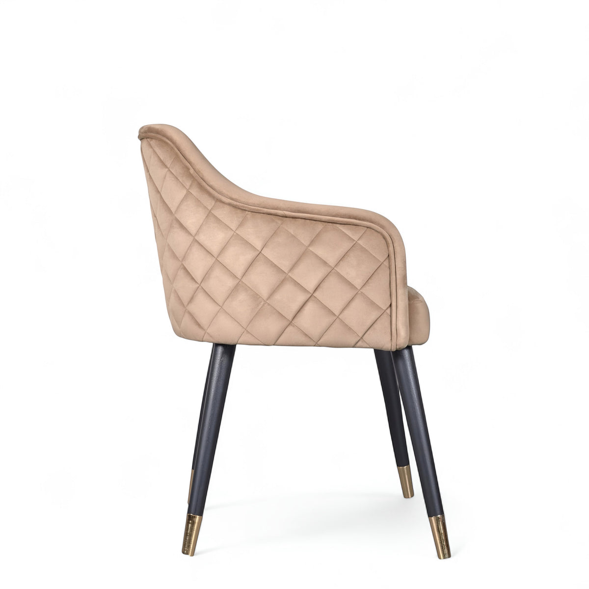 Side view of the Vaya Home Pino dining chair with beige upholstery, curved arm detail, and black tapered legs with gold caps.