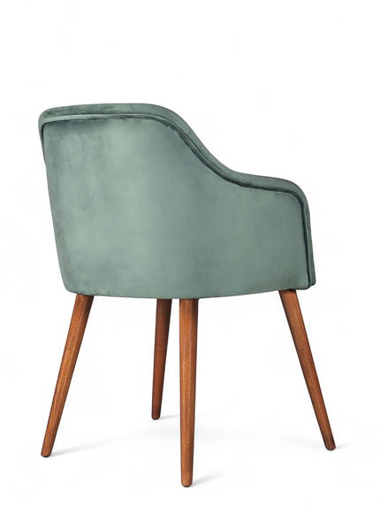 Rear angled view of the Vaya Home Pino dining chair featuring green velvet upholstery, a softly curved back, and tapered wood legs.