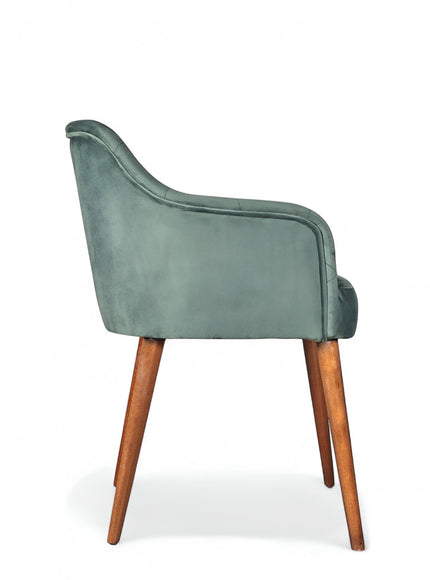 Side view of the Vaya Home Pino dining chair with green velvet upholstery, curved arm detail, and tapered wood legs.