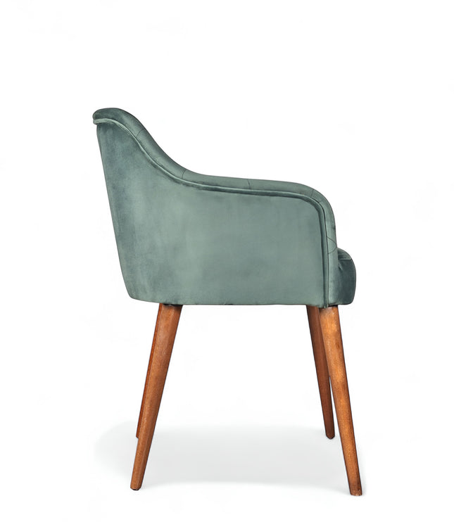 Side view of the Vaya Home Pino dining chair with green velvet upholstery, curved arm detail, and tapered wood legs.