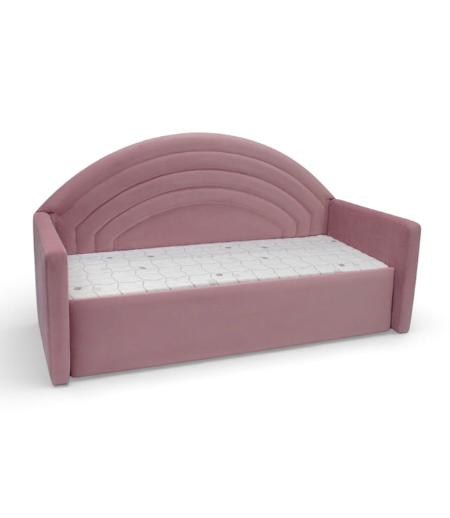 Angled front view of the Vaya Home Rainbow kids bed with pink upholstery, side arms, and an arched rainbow-style headboard.