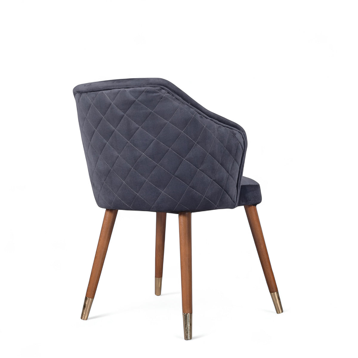 Rear angled view of the Vaya Home Rioga dining chair featuring dark blue velvet upholstery, diamond-quilted back detail, and tapered wood legs with gold caps.