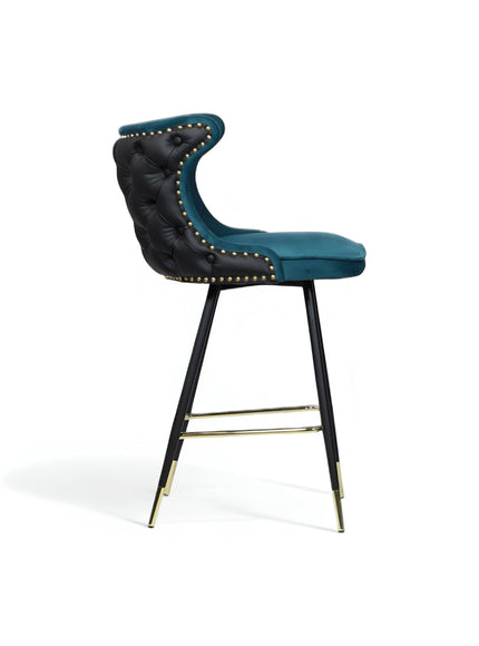 Side view of the Vaya Home Roket bar stool with blue seat upholstery, black button-tufted back, nailhead trim, and black metal legs with gold accents.