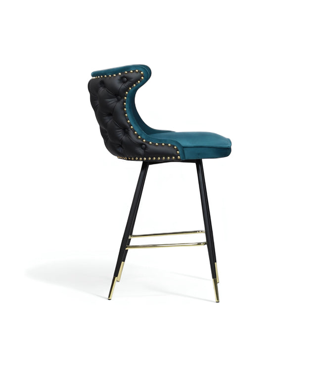 Side view of the Vaya Home Roket bar stool with blue seat upholstery, black button-tufted back, nailhead trim, and black metal legs with gold accents.