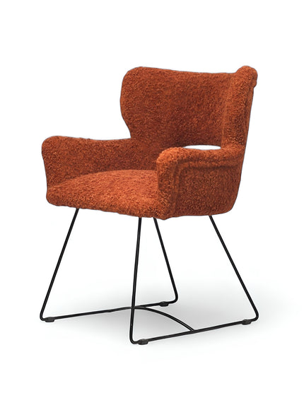 Front angled view of the Vaya Home Rolf accent chair with orange boucle upholstery, sculpted arms, and a black metal sled base.