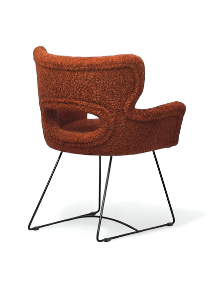Rear angled view of the Vaya Home Rolf accent chair featuring orange boucle upholstery, an open back detail, and a black metal sled base.