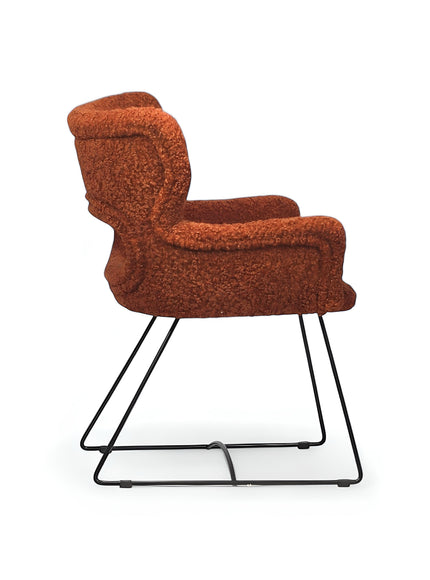 Side view of the Vaya Home Rolf accent chair with orange boucle upholstery, sculpted arms, and a black metal sled base.