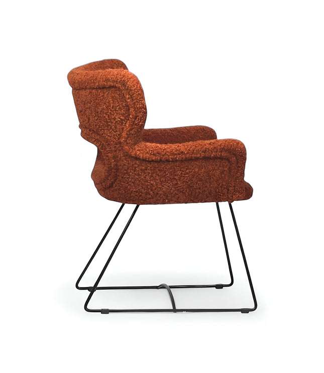 Side view of the Vaya Home Rolf accent chair with orange boucle upholstery, sculpted arms, and a black metal sled base.