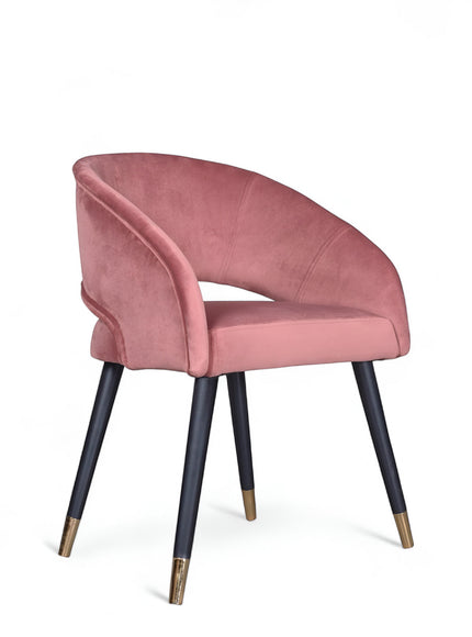 Front angled view of the Vaya Home Rosado dining chair with pink velvet upholstery, curved arm detail, and black legs with gold caps.