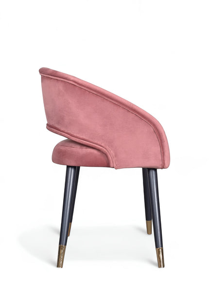 Side view of the Vaya Home Rosado dining chair with pink velvet upholstery, curved backrest, and black legs with gold caps.