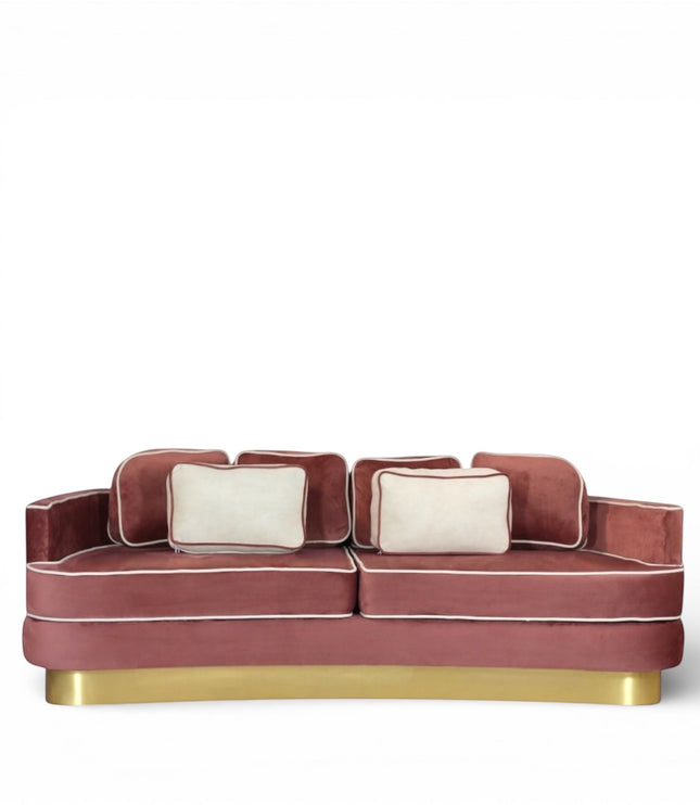 Front view of the Vaya Home Rose curved sofa with pink velvet upholstery, accent cushions, contrast piping, and a gold base.