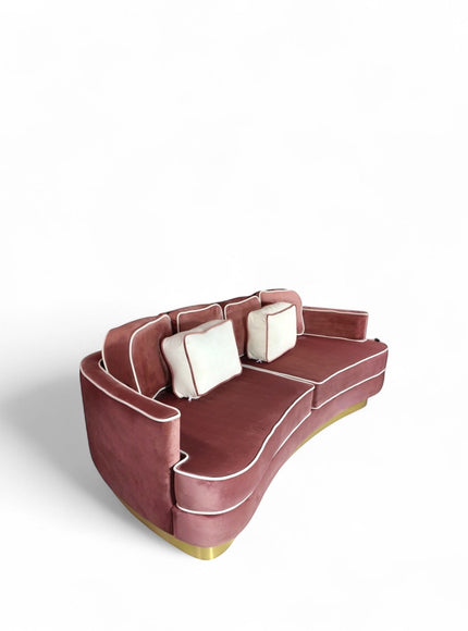 Rear angled view of the Vaya Home Rose curved sofa showing its rounded back, pink velvet upholstery, and gold base detail.